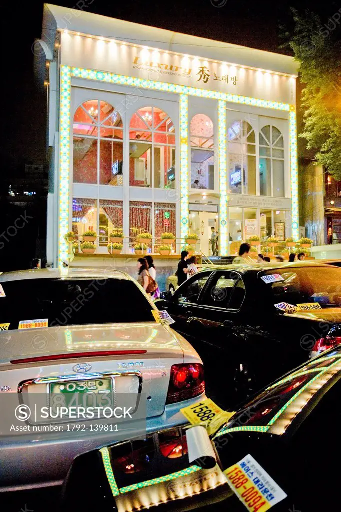 South Korea, Seoul, Hongdae District, front view of a luxury karaoke nolaebang with views to the outside and Korean brand cars Hyundae in the foregrou...