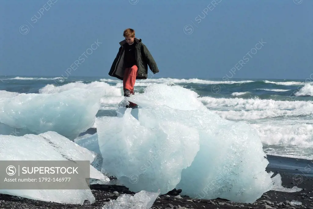 Iceland, Austurland Region, child on iceberg failed on a volcanic beach, in rising tide, next to the Jokulsarlon Glacial Lake