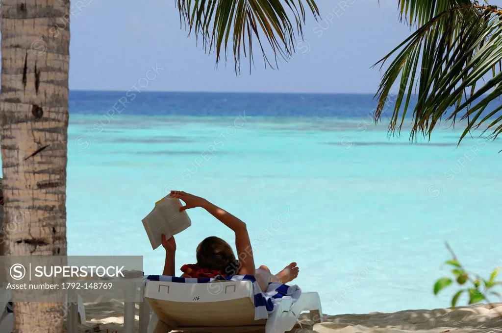 Maldives, North Male Atoll, Thulhagiri Island, Thulhagiri Resort and Spa, a tourist on holidays reading a book under a palm tree shade