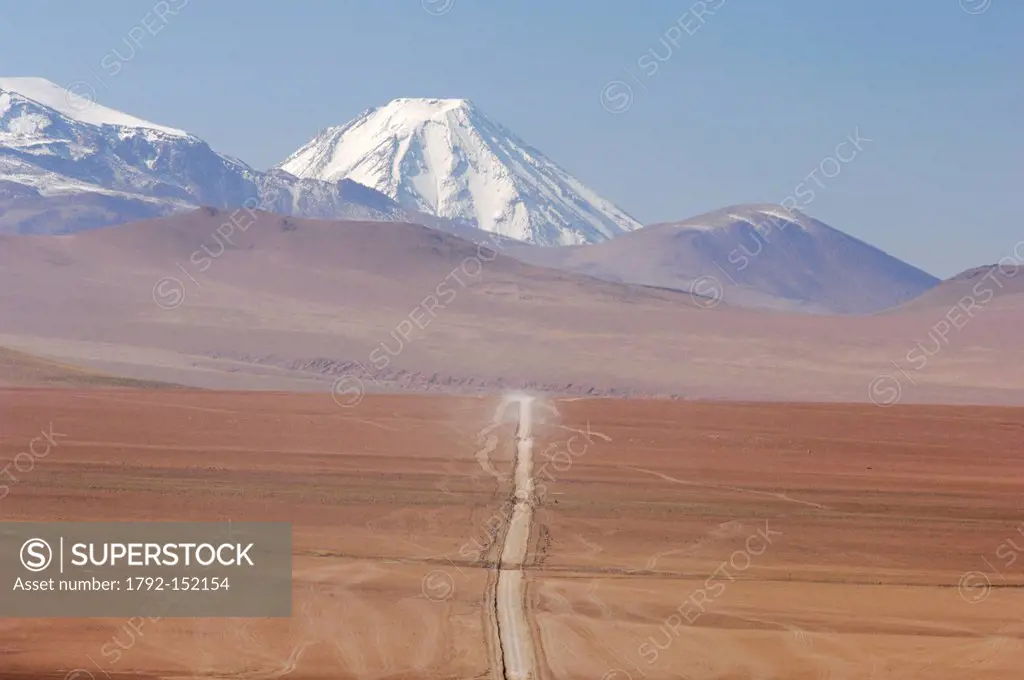 Chile, Antofagasta region, Altiplano, road or dirt track in the Altiplano in the background with the volcanoes of the Andes
