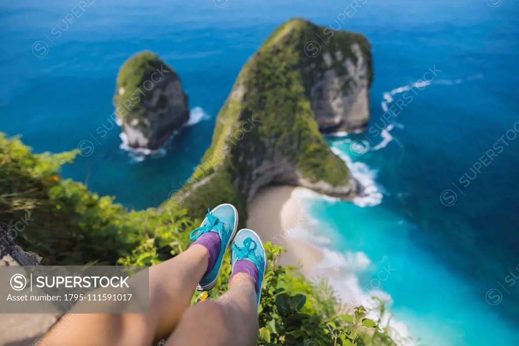 Legs of woman sitting above Kelingking Beach in Nusa Penida, Indonesia