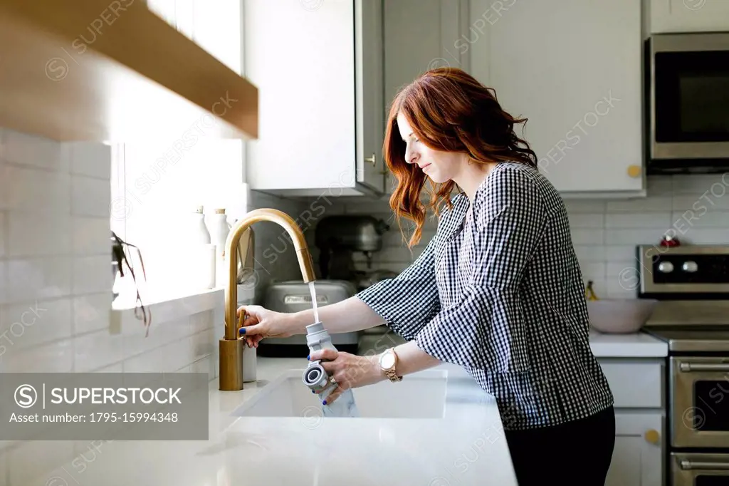 Woman filling water bottle in kitchen sink