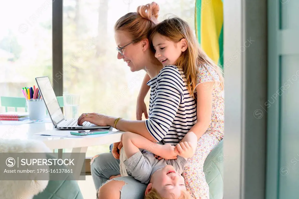 Children (4-5, 6-7) climbing on their mother while she works from home