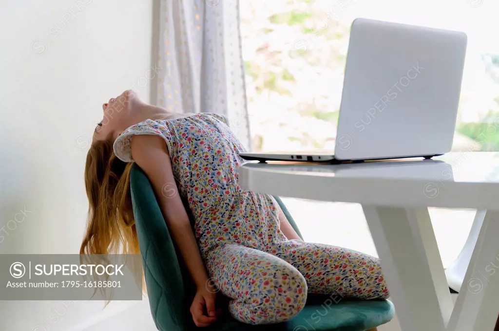 Girl (6-7) leaning back on chair while remote learning