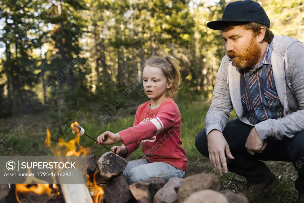 Man with daughter (6-7) roasting marshmallow above campfire, Wasatch Cache National Forest