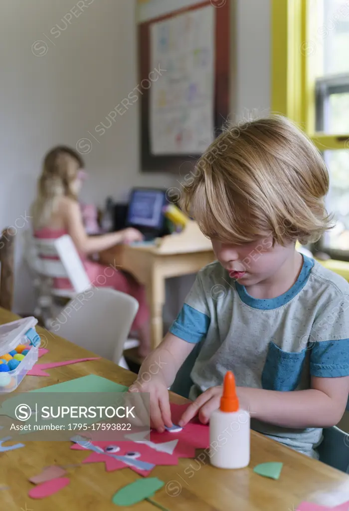 Boy (4-5) preparing paper cutout, girl (6-7) in background