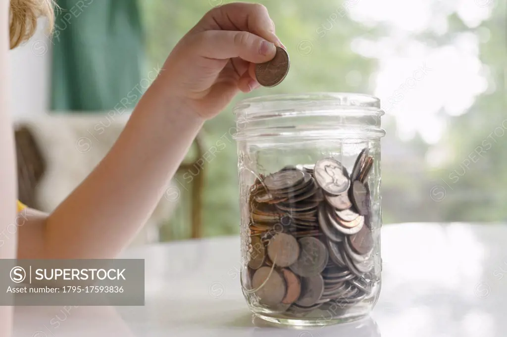 Boys (4-5) hand putting coins into jar
