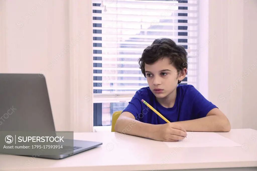 Boy (8-9) sitting at desk at home during remote lesson
