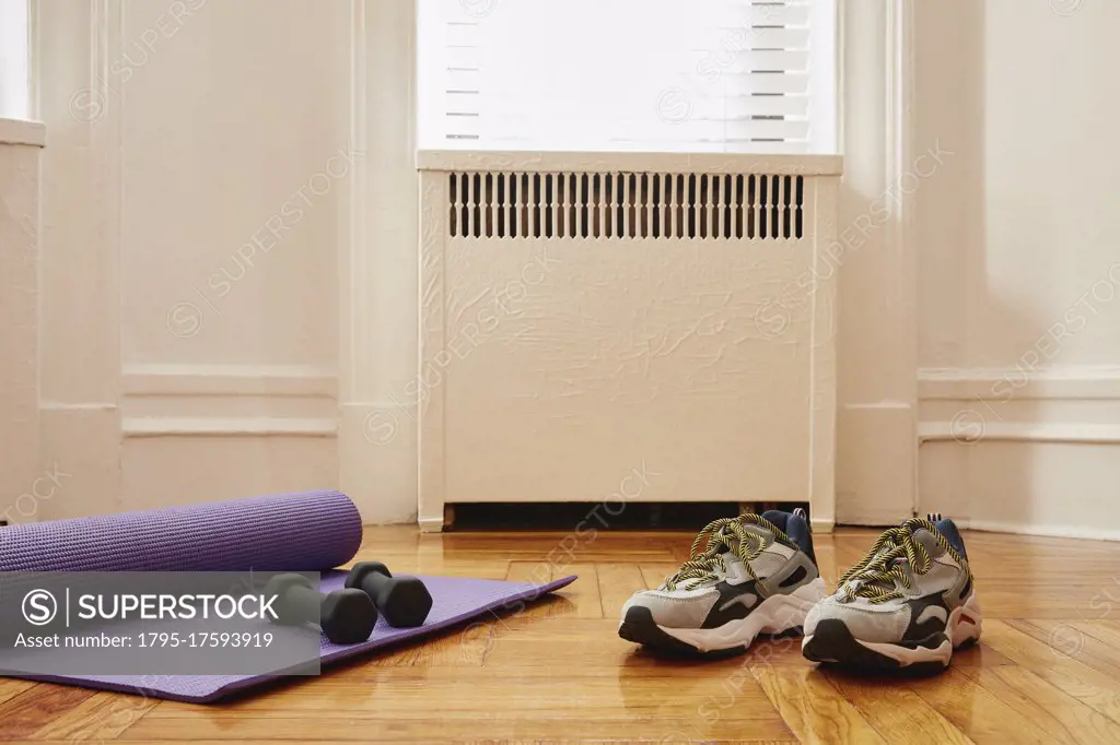 Yoga mat, weights and sports shoes on floor at home gym