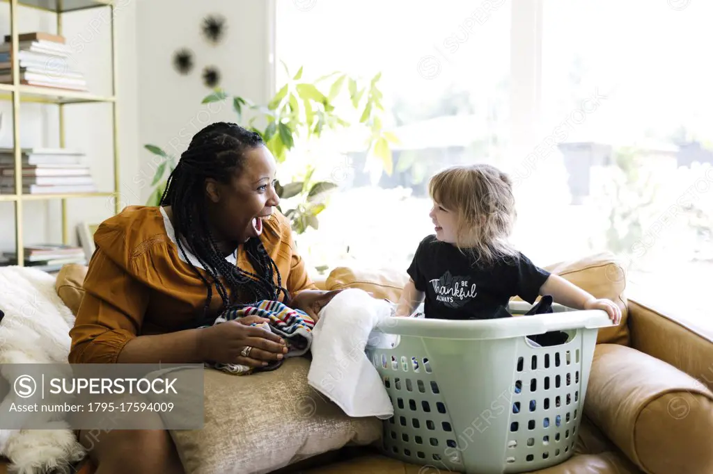 Woman playing with little girl (2-3) sitting in laundry basket
