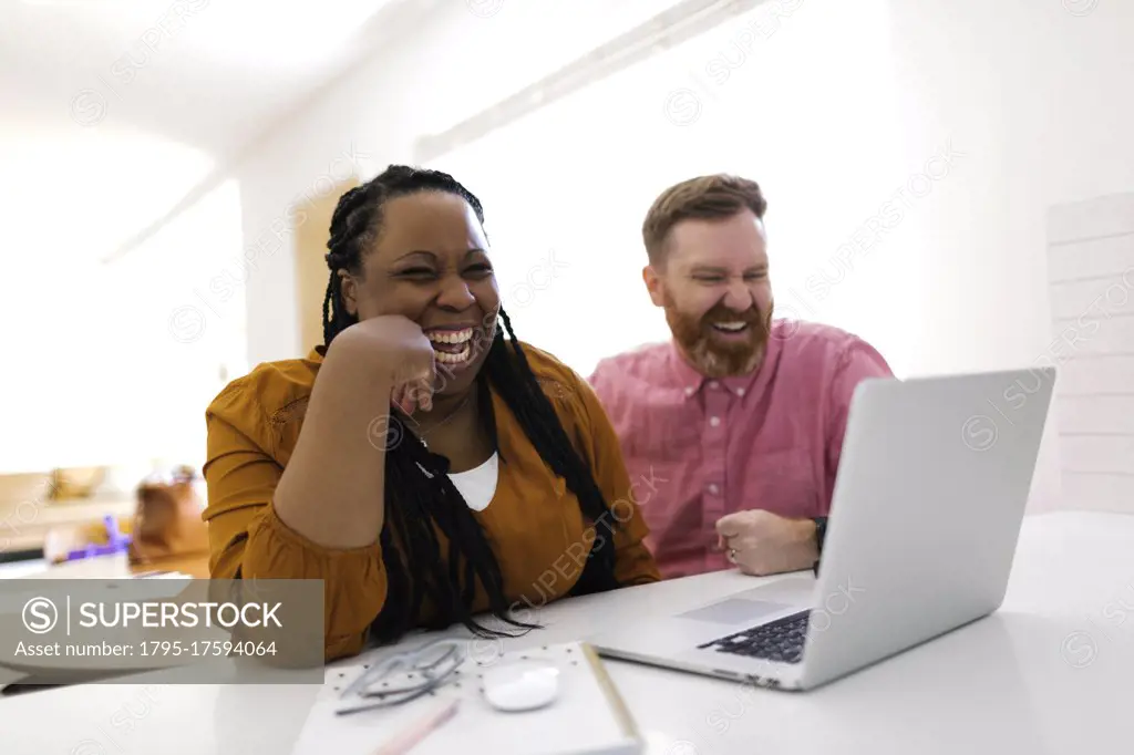 Smiling man and woman looking at laptop at desk in home office