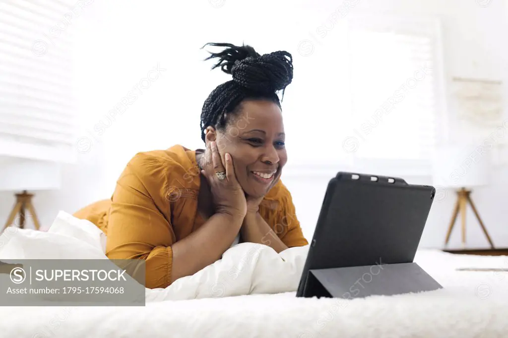 Smiling woman lying on bed and looking at tablet