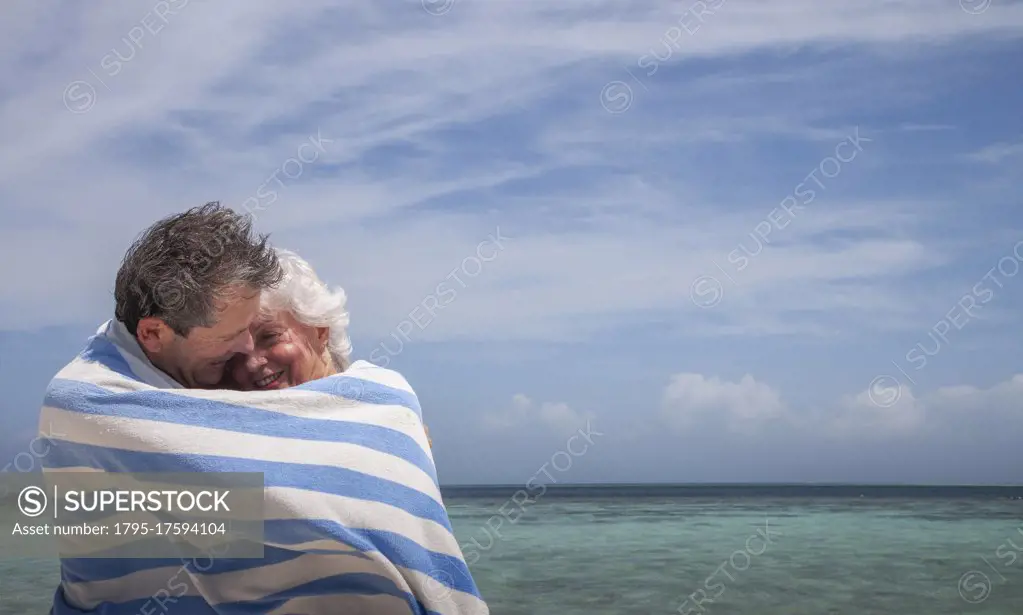 Indian Ocean, Maldives, Ari Atoll, Vilamendhoo Island, Happy couple wrapped in striped beach towel on tropical beach