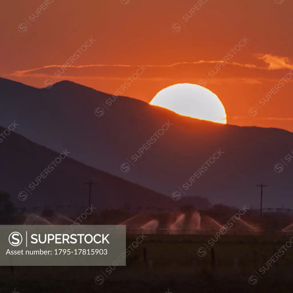USA, Idaho, Bellevue, Irrigation equipment in field and sun setting behind mountain