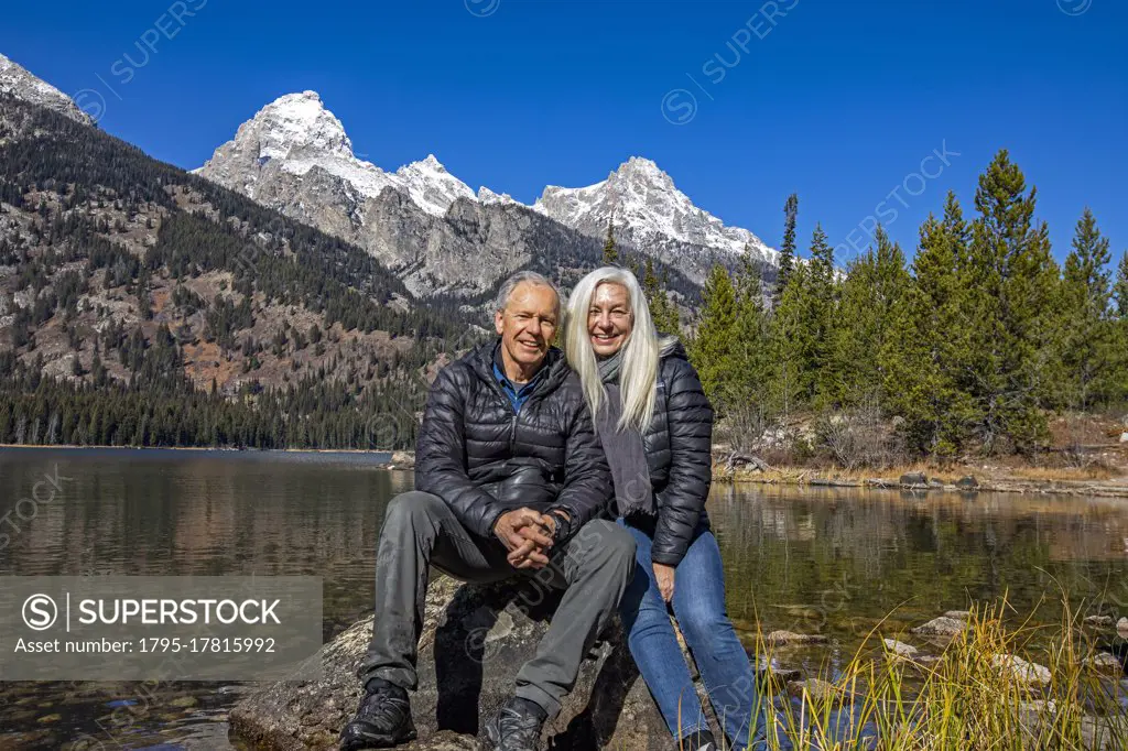 USA, Wyoming, Jackson, Grand Teton National Park, Outdoor portrait of senior couple sitting on rock by Taggart Lake in Grand Teton National Park