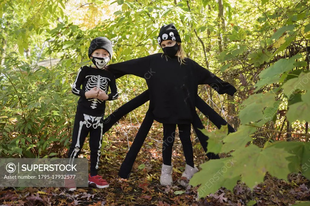 Girl (8-9) and boy (6-7) wearing Halloween costumes in forest