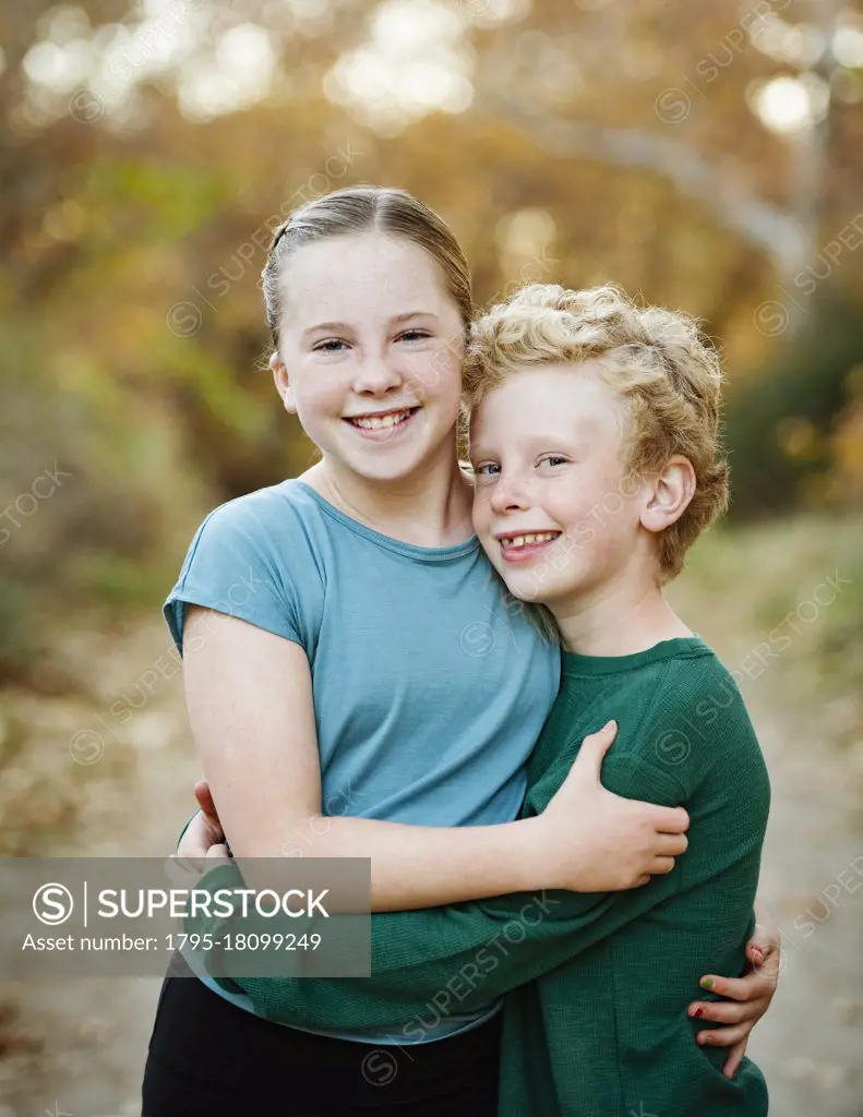 United States, California, Mission Viejo, Portrait of smiling brother (10-11) and sister (12-13) embracing in forest