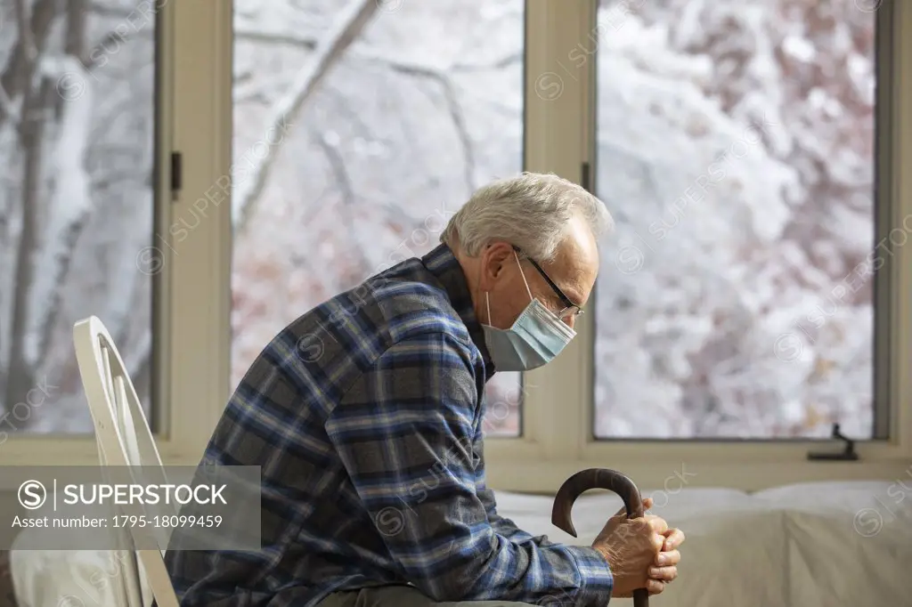 Senior man wearing protective mask sitting near window