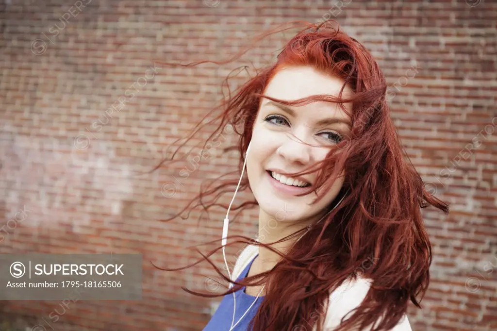 Young woman with long red hair, wearing earphones, close-up
