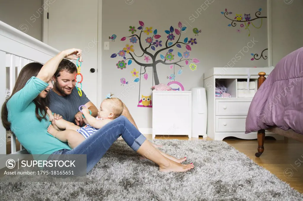 Mid adult couple playing with baby toy and baby daughter on lap