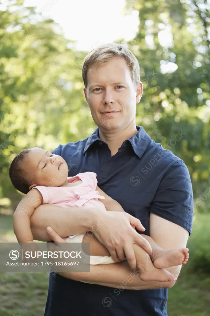 Father outdoors holding baby girl looking at camera smiling