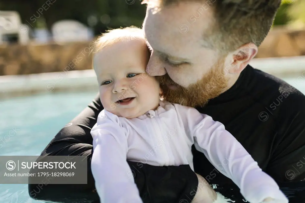 Father embracing baby son (12-17 months) in swimming pool