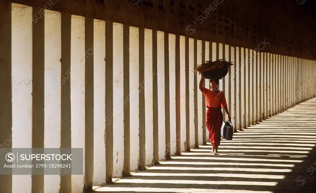 Myanmar, Bagan, Mandalay Division, Woman walking in portico of Schwezigon Pagoda carrying wood on her head