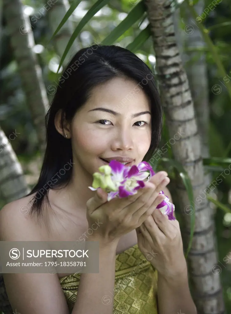 Thailand, Koh Samui Island, Portrait of smiling woman smelling orchids