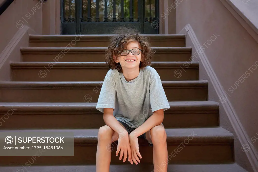 USA, New York, New York City, Boy sitting on steps in front of building