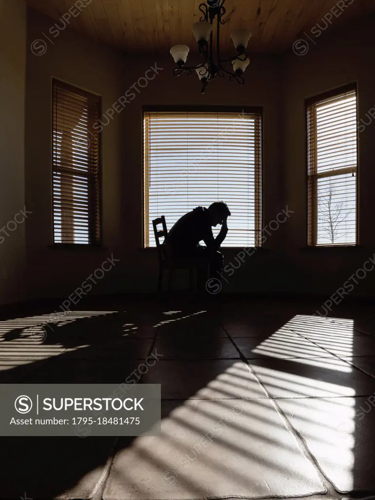 Silhouette of depressed man sitting on chair in living room