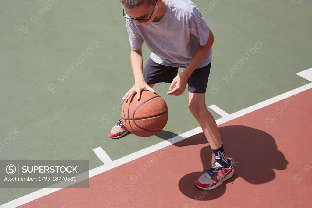 Boy (8-9) dribbling basketball in park