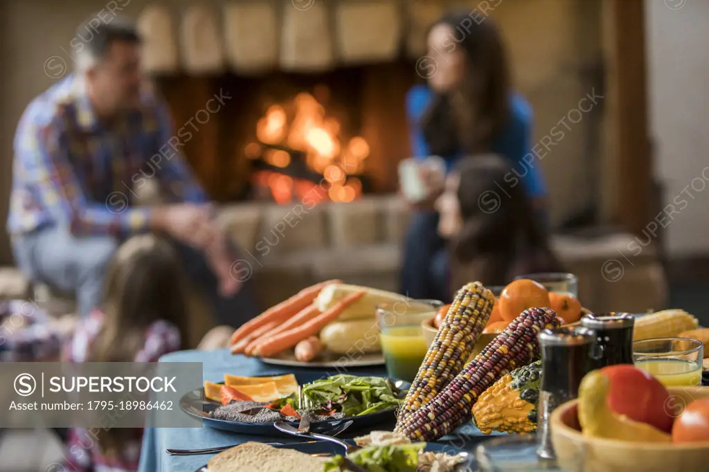 Dinner on table and family with children (10-11, 12-13, 16-17) sitting by fireplace