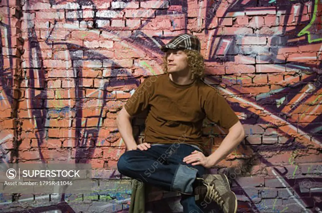 Young man sitting in front of graffitied wall