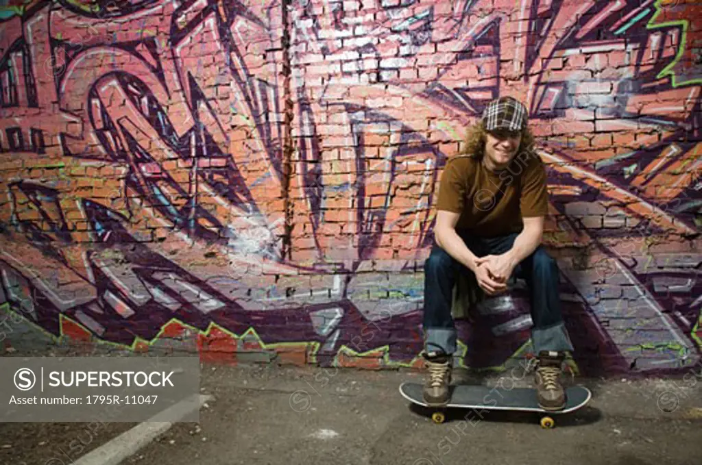 Young man with skateboard in front of graffitied wall