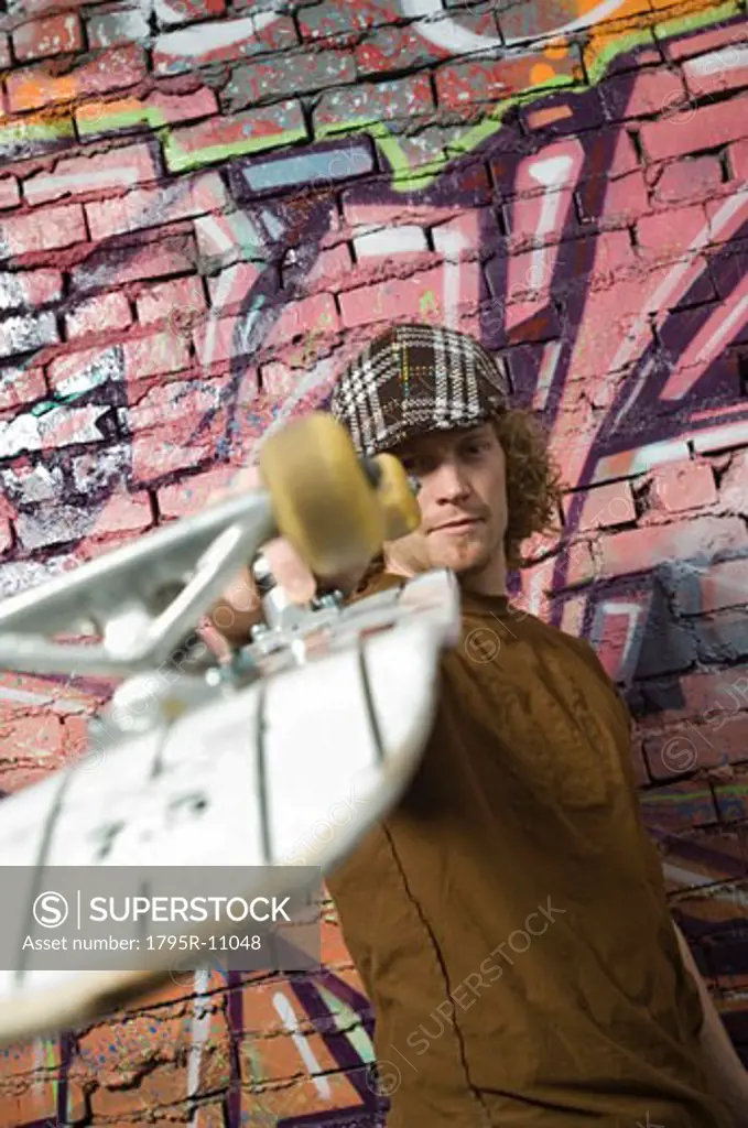 Young man with skateboard in front of graffitied wall
