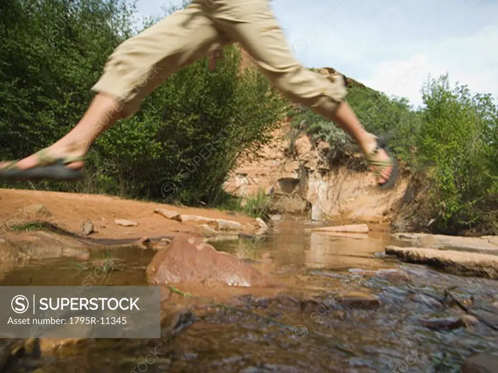 Woman jumping over stream
