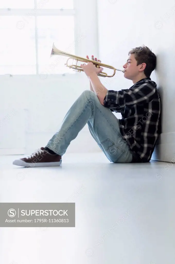 Teenage boy (16-17) playing trumpet in hallway