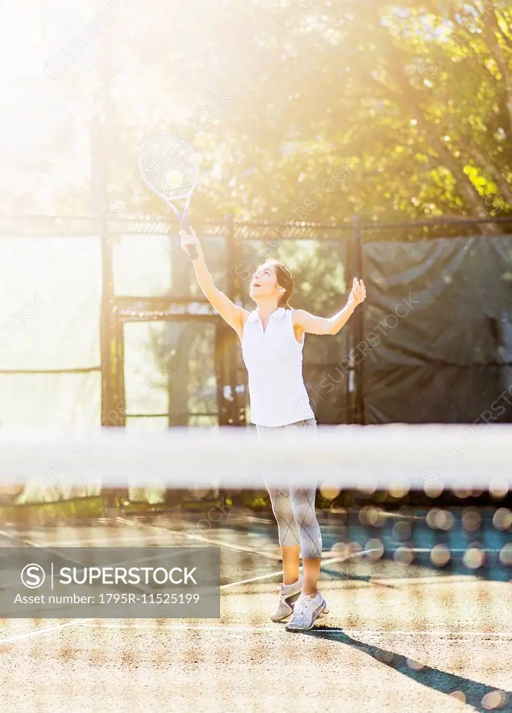Young woman in tennis court about to serve ball with net in blurred foreground
