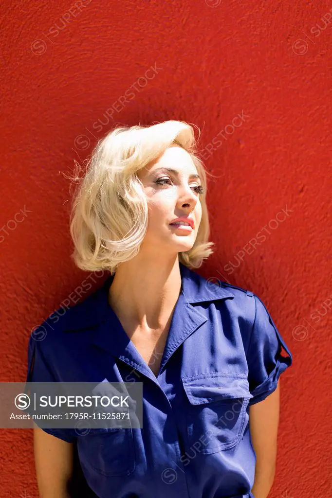 Close-up of Woman in blue dress posing against red wall in sunlight