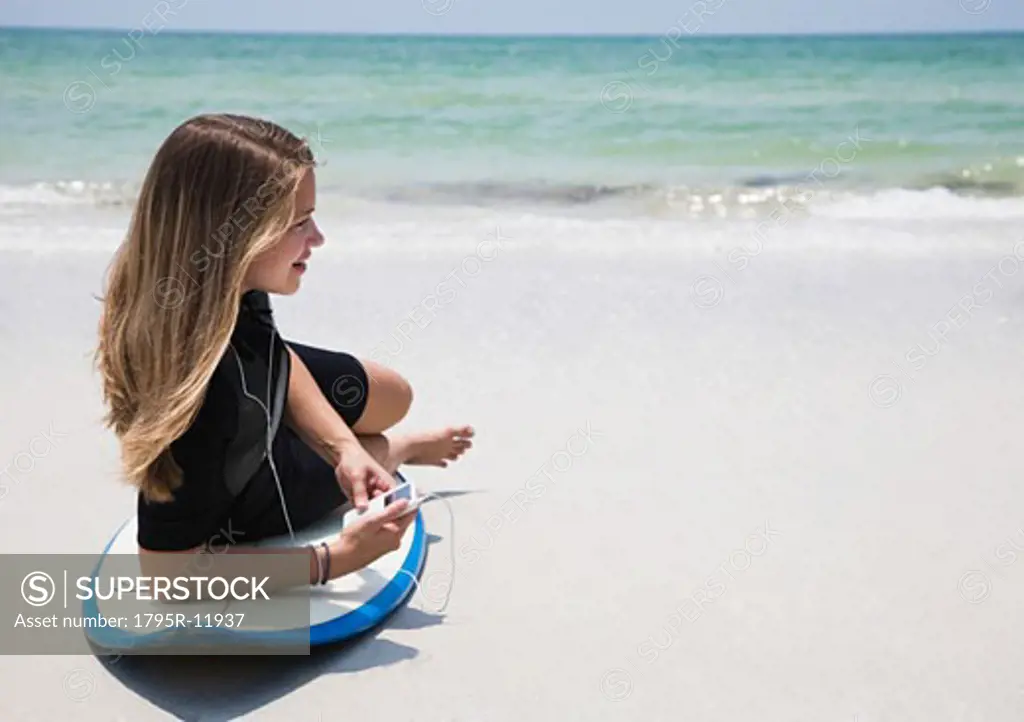 Girl listening to mp3 player on surfboard, Florida, United States