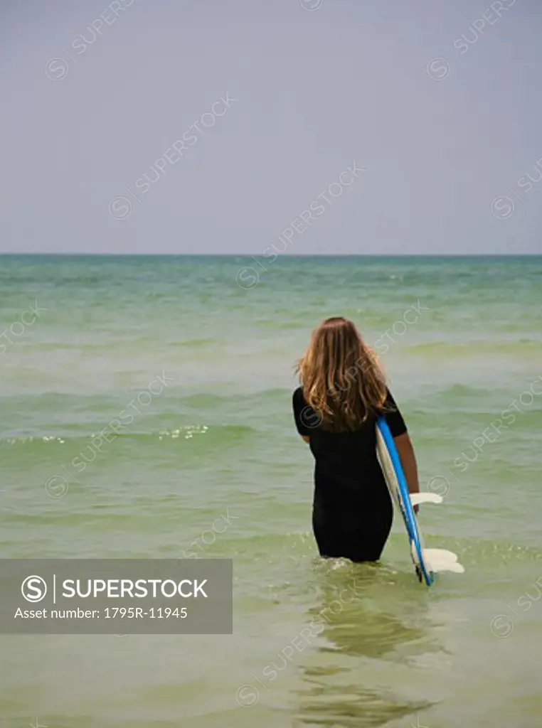 Girl walking into water with surfboard, Florida, United States
