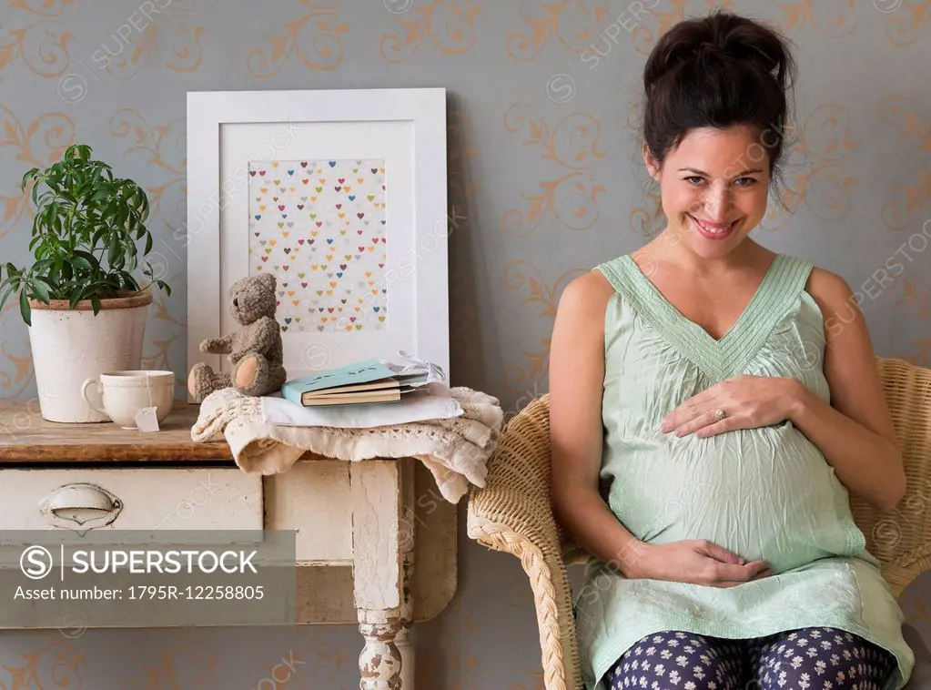 Pregnant woman sitting in chair touching abdomen smiling