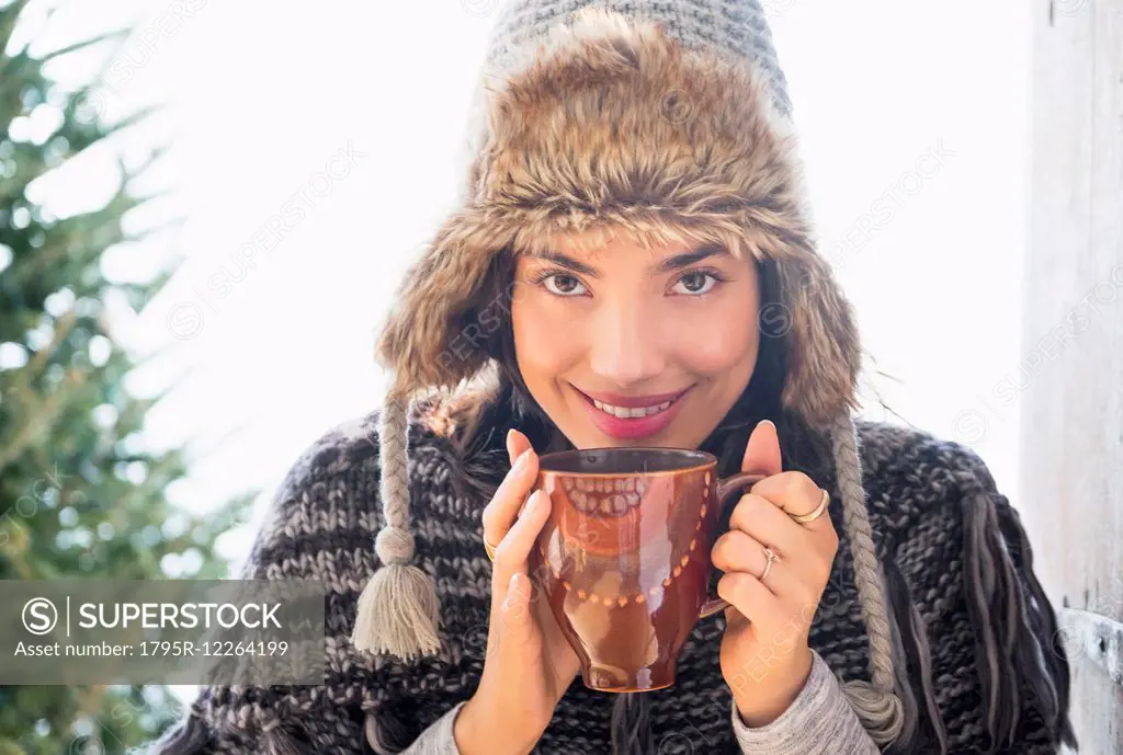 Portrait of young woman wearing winter hat, holding mug