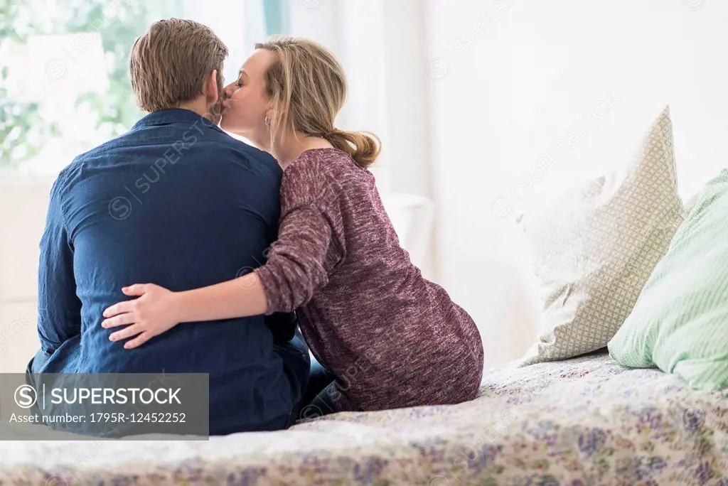 Rear view of woman kissing man on cheek on bed