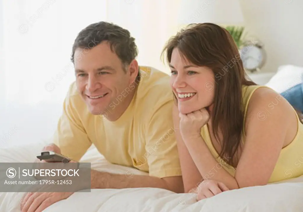 Couple pointing remote control on bed