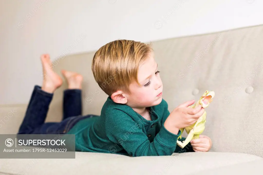 Boy (2-3) playing with toy dinosaur on sofa