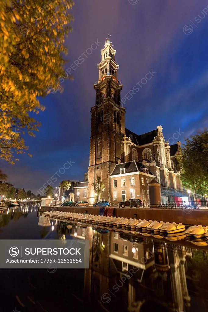 Illuminated Westerkerk Church reflecting in still canal