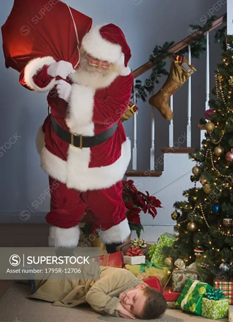 Santa Claus looking at boy sleeping next to Christmas tree