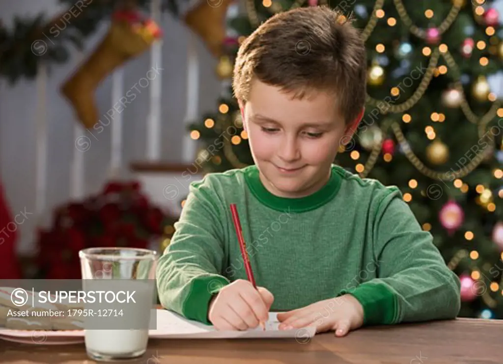 Boy writing letter in front of Christmas tree