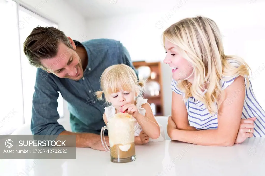 Girl (2-3) drinking milkshake with parents at home